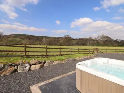 a hot tub on a gravel road next to a field at Beudy Bach Barn in Llanuwchllyn