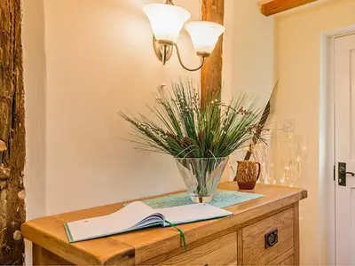 a table with a book and a vase with a plant on it at Borrowers Cottage in Condover