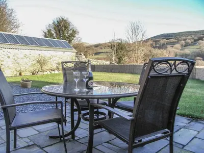 a glass table with two chairs and a bottle of beer at Y Bwythyn at Henfaes in Rhydymain