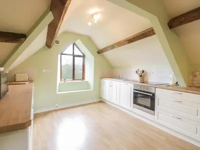 an attic kitchen with white cabinets and a window at Hen Ysgubor Cottage in Bala