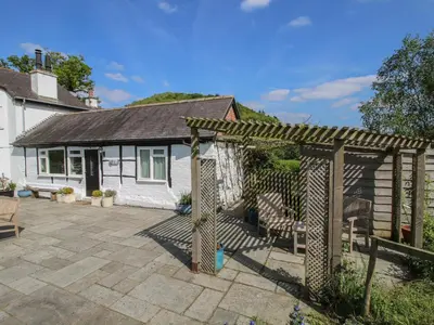a backyard with a pergola and chairs and a house at The Old Beams at Pont y Forwyn in Llansantffraid-ym-Mechain