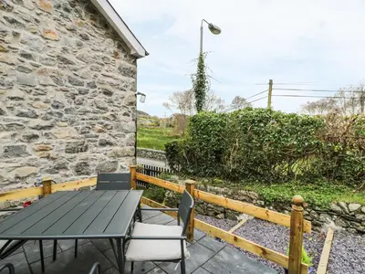 a patio with a table and chairs and a stone wall at Llwyn Celyn in Llanfachreth
