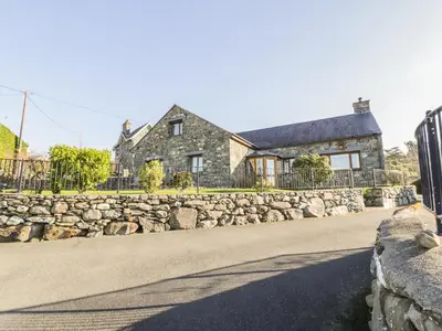 a stone house with a stone wall and a fence at Awel Y Llan in Llanfair