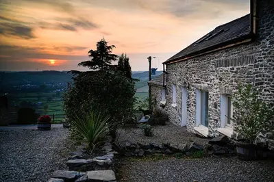 a stone house with a sunset in the background at Coedmor Cottages in Lampeter