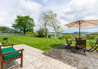 a patio with a table and chairs and an umbrella at Bwthyn Bryn yr Aber in Bala