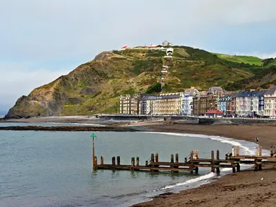 a beach with a pier and buildings on a hill at No 2 Pegraig Draw - Uk6435 in Llanychaiarn