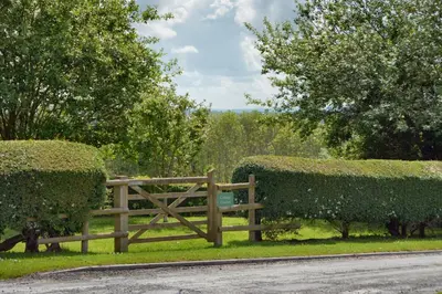 a wooden fence in the grass next to some bushes at Upper Onibury Cottages in Onibury