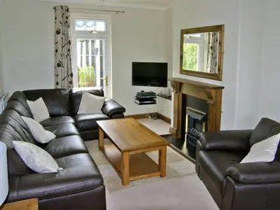 a living room with a leather couch and a table at Railway Cottage in Fairbourne
