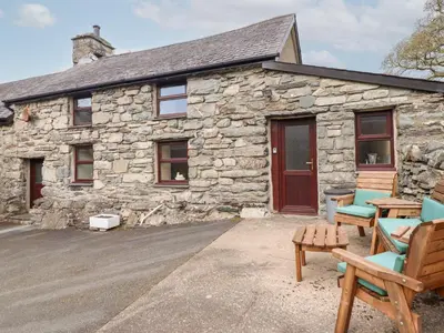 a stone cottage with two chairs and a bench at Y Bwthyn in Llanbedr