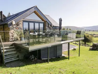 a house with a deck with a table and chairs at Tyn Llwyn in Gwyddelwern