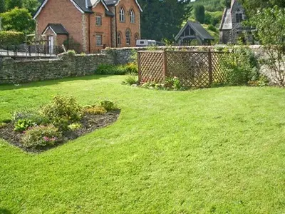 a yard with green grass and a brick house at Tailor's Cottage in Abbey-Cwmhir