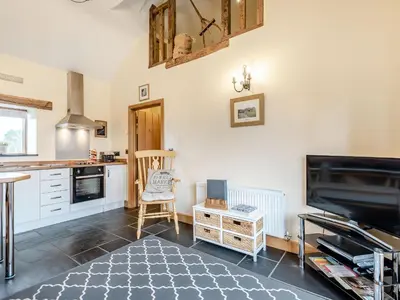 a kitchen with white cabinets and a tv and a table at The Granary in Llanfair Caereinion