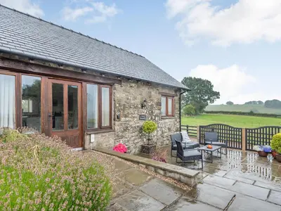 a stone cottage with a patio and a table and chairs at The Granary in Llanfair Caereinion