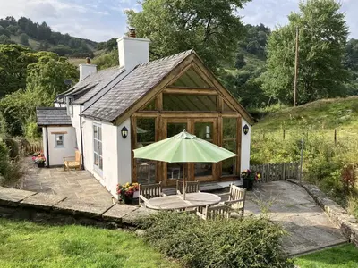 a small cottage with a table and a green umbrella at Pen Y Bont in Llangollen