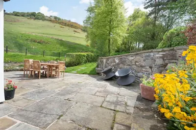 a patio with a table and chairs and a stone wall at Pen Y Bont in Llangollen