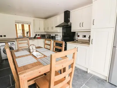a kitchen with white cabinets and a wooden table and chairs at Tynddol Barn in Llanbadarn-fynydd
