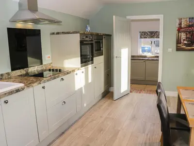 a kitchen with white cabinets and a wooden floor at Swallow Barn in Walford