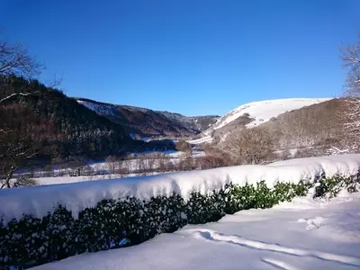 a snow covered field with a river in the distance at Kilsby Cottage in Llanwrtyd Wells