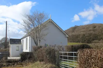 a white house with a hill in the background at Capel- Y-Bryniau in Pennal