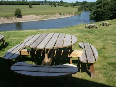 a wooden picnic table with a bench and a river at The Corbet Arms in Shrewsbury
