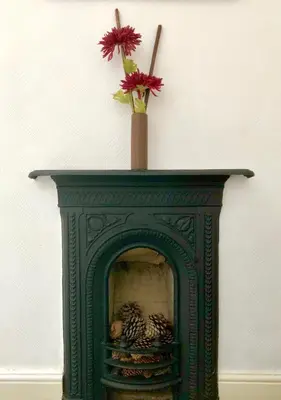 a green fireplace with a vase with flowers on top at Plough and Harrow in Brecon