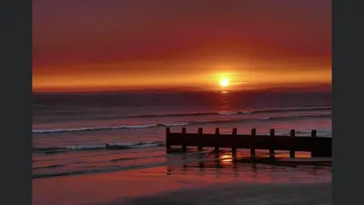 a sunset over the ocean with a pier on the beach at Endeavour Guest House in Barmouth