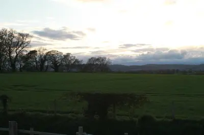 a field with a fence and trees in the distance at Off the Rails in Oswestry