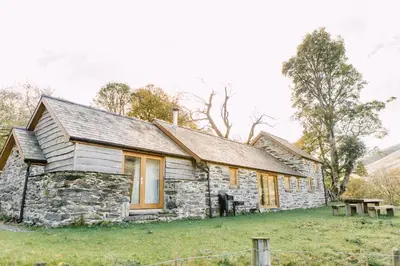 an old stone house in a field with picnic tables at Glyn Mawr Barn in Bala