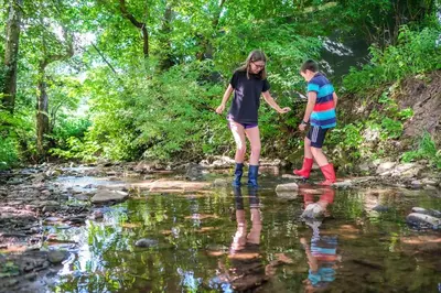 two people crossing a stream in the water at Wye Glamping in Velindre