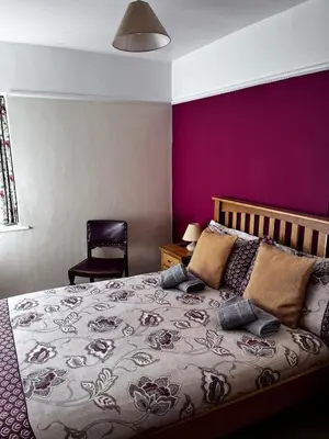 a bedroom with a bed with a purple wall at The Moorings in Fairbourne