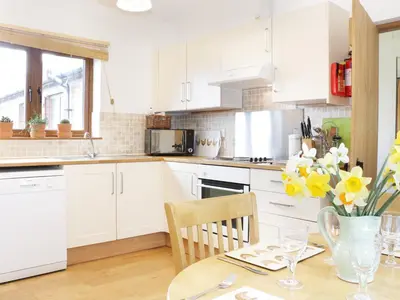 a kitchen with white cabinets and a table with yellow flowers at Acorn Cottage 1 in Petton
