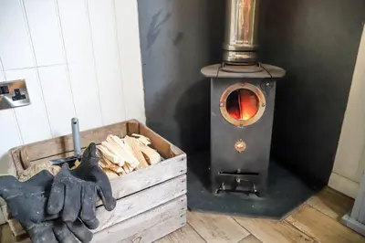 a stove with a wooden box and a pair of gloves at Nant Cafn - Hafan Hideaways Eryri in Machynlleth