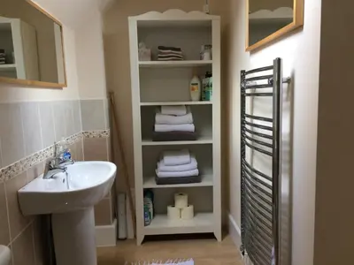 a bathroom with a sink and a white shelf with towels at Berries Coach House in Church Stretton