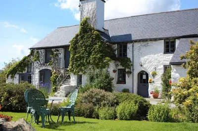 a white house with two chairs in the yard at Dolgun Uchaf Historic B&B and Cottages with Boutique Bedrooms In The Heart of Snowdonia in Dolgellau