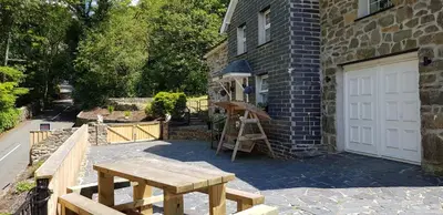 a wooden table next to a building with a white door at Hilltop Cottage/ Penrhiw in Maentwrog
