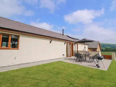 a house with a patio with chairs and a grill at Pentre Fach in Llanddewi Ystradenny