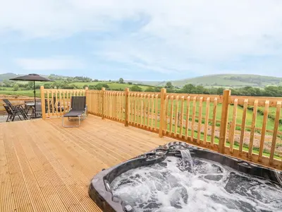 a hot tub on a deck with a wooden fence at Pentre Fawr in Llanddewi Ystradenny