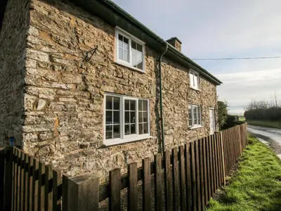 a stone house with white windows and a fence at Bicton Cottage in Acton