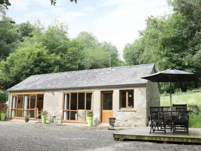 a small stone cottage with a table and an umbrella at Woodpecker Cottage in Ludlow