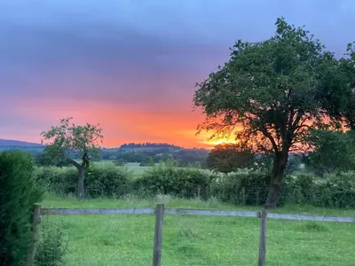 a sunset in a field with a fence and a tree at Ludlow Vintage Airstream in Ludlow