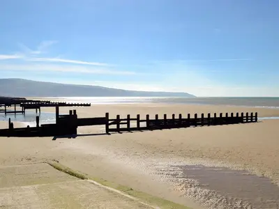 a beach with a pier and the ocean at Y Gweithdy in Barmouth
