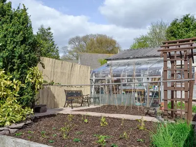 a glass greenhouse in a garden with a bench at Three Views Bungalow in Talgarth
