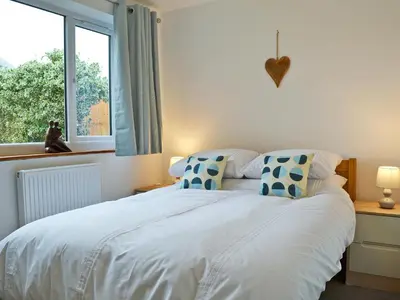 a bedroom with a white bed with blue pillows and a window at Lle Clyd in Harlech