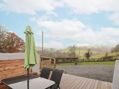 a patio with a table and a green umbrella at Rhianwen, Plas Moelfre Hall Barns in Llangadwaladr