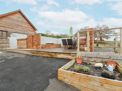 a backyard with a wooden deck with a table at Rhianwen, Plas Moelfre Hall Barns in Llangadwaladr
