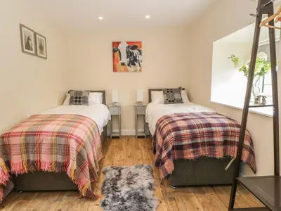 a bedroom with two beds and a rug on the floor at Rhianwen, Plas Moelfre Hall Barns in Llangadwaladr