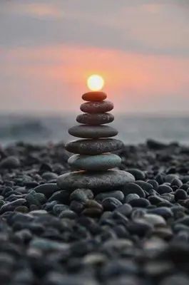 a stack of rocks on a pebble beach with the sunset at Hendre Coed Isaf Caravan Park in Barmouth