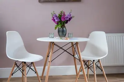 a table with three white chairs and a vase with purple flowers at The Hayloft, Wall End Farm in Leominster