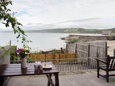 a table with a plate of food on a balcony with the water at Seadrift in New Quay