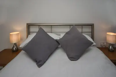 two gray pillows on a white bed with two lamps at Parc y Bryn Serviced Apartments in Aberystwyth